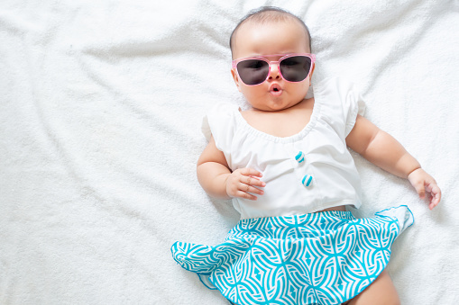 Asian baby girl wearing swimming suit and pink sunglasses on white background, baby in beach wear fashion