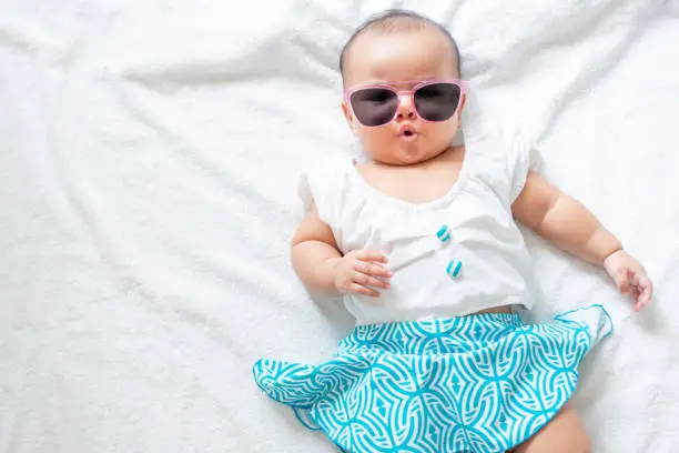 Photo of Asian baby girl wearing swimming suit and pink sunglasses on white background, baby in beach wear fashion