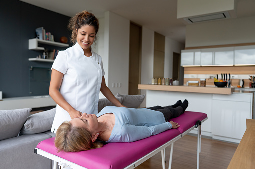 Latin American freelance masseuse giving a massage to a customer at home on a stretcher â indoor spa concepts