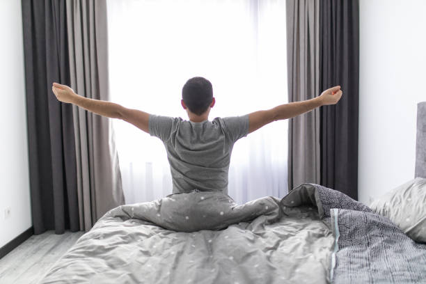 istock Handsome young man waking up in bed and stretching his arms 1151440078