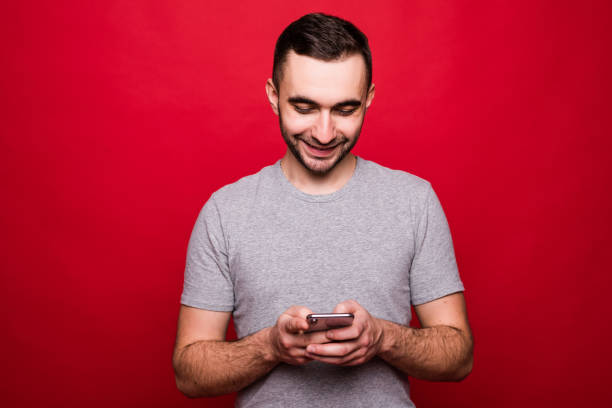 istock Portrait of a smiling young man using mobile phone isolated over red background 1151441128