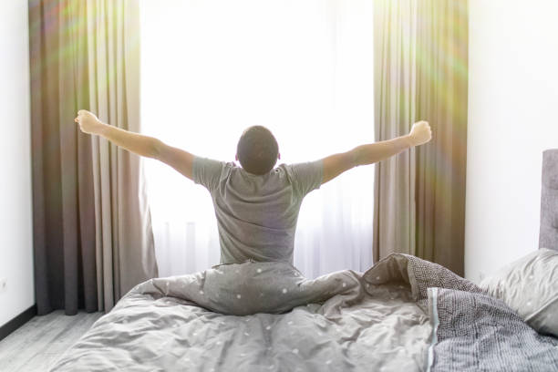 istock Handsome young man waking up in bed and stretching his arms. Rear view. 1151442922