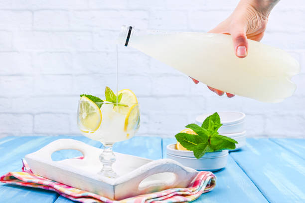 Lemonade with ice and lemon slices and mint in a glass on a blue wooden table. Summer cold refreshing drink with fruits and vitamins.