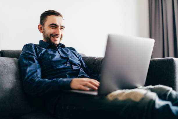 istock Young handsome man with modern laptop on sofa at home 1151445867