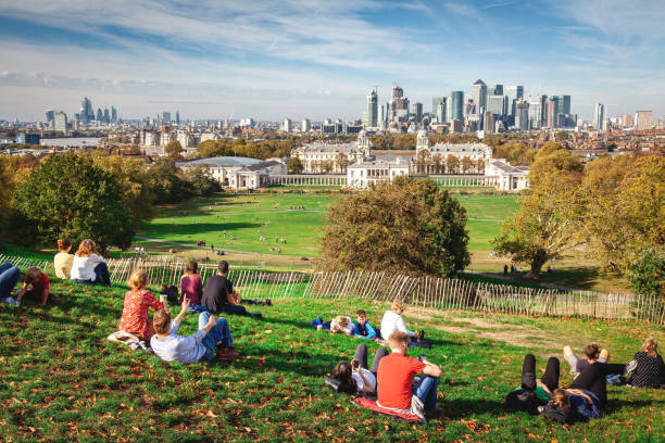 Relaxing in Greenwich Park overlooking London London, United Kingdom - October 13, 2018: Relaxing in Greenwich Park overlooking London. Young people relax in Greenwich Park on a summer afternoon and await the sunset. Greenwich Park is the oldest enclosed Royal Park and is situated on a hilltop, it has great views over London including the Naval College, Canary Wharf, the Millennium Dome and the skyscrapers of the city of London. queen's house stock pictures, royalty-free photos & images