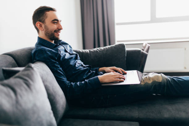 istock Young handsome man with modern laptop on sofa at home 1151447303