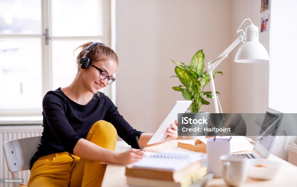 Молодая студентка сидит за столом, используя планшет во время учебы. - Стоковые фото Обучение роялти-фри