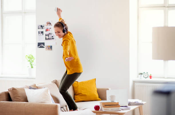 A young female student with headphones dancing on sofa when studying.