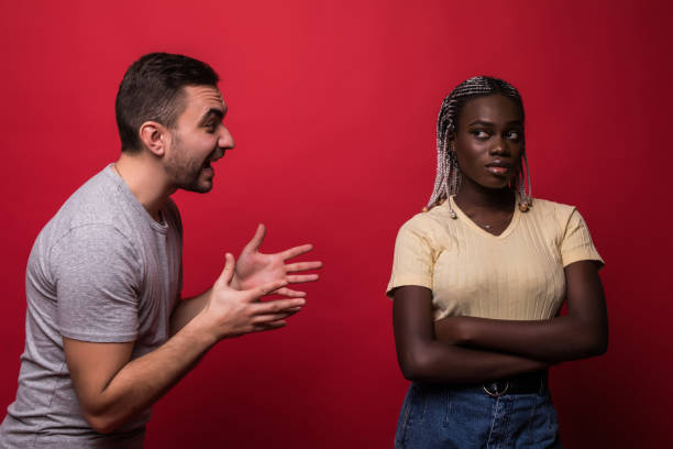 istock Young mixed race couple having a quarrel. Girl is looking at camera while guy is scolding her isolated on red background 1151456030
