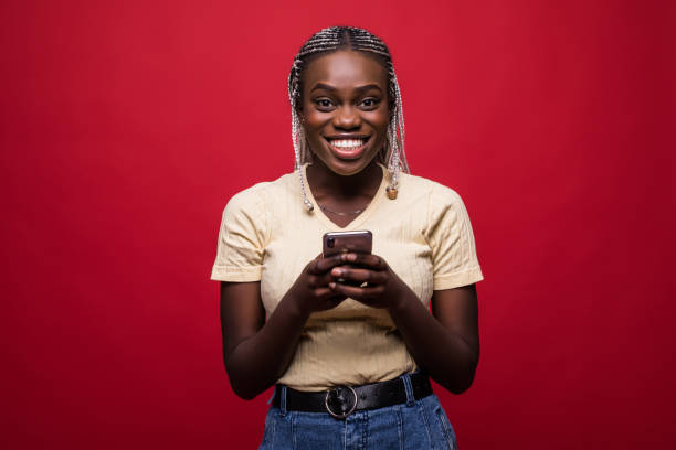 istock Happy young african woman use mobile phone casually dressed standing isolated over red background 1151456535