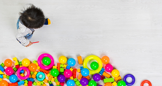 Young Asian kid playing among several kinds of  colorful toys, taken form high angle.
