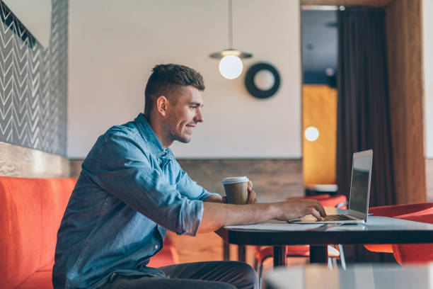 istock Young man using laptop in the cafe and looking glad 1151466850