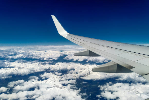 mountains and white snow on the tops under the wing of the aircraft during the flight - mountain range earth sky airplane imagens e fotografias de stock