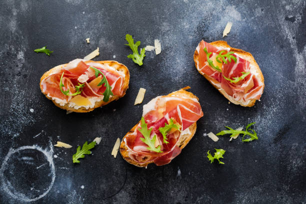 abra sándwiches con jamón, rúcula y queso duro sobre un fondo oscuro y viejo de hormigón. estilo rustik. vista superior. - serrano chilli pepper meat ham spain fotografías e imágenes de stock