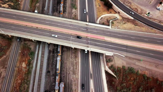 Drone Footage Of An Overpass Of A Four-Lane Parkway That Runs Along Side A Railroad Yard With Many Old Abandon Train Engines