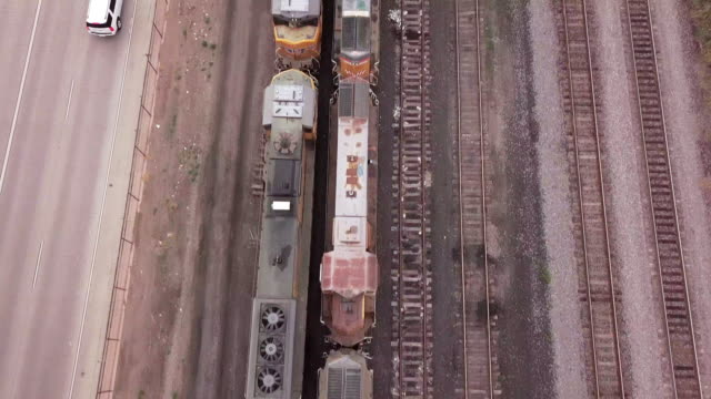 Drone Footage Of An Overpass Of A Four-Lane Parkway That Runs Along Side A Railroad Yard With Many Old Abandon Train Engines