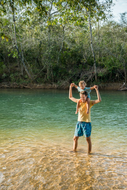 Young man carrying son on his shoulders standing in river_