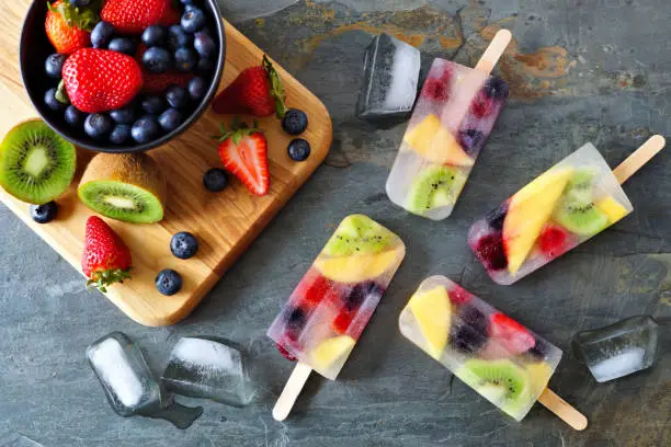 Photo of Healthy fruit summer ice pops, top view scene on a dark background