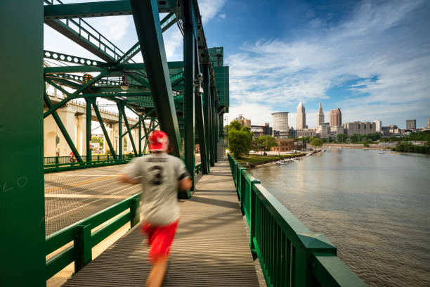 Downtown Cleveland city skyline in Ohio USA Man jogs over the bridge of the Cuyahoga river by the downtown skyline view of Cleveland Ohio USA cuyahoga river photos stock pictures, royalty-free photos & images