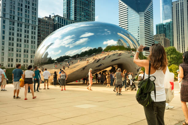 People gather around the Cloud Gate Bean and Chicago Skyline in summer Chicago, Illinois, USA - September 20, 2018: People gather around the Cloud Gate sculpture and downtown Chicago skyline.  Cloud Gate is also known as "The Bean" because of its shape is located in Millennium Park in Chicago.  Cloud Gate is a public sculpture by British artist Anish Kapoor. millennium park stock pictures, royalty-free photos & images