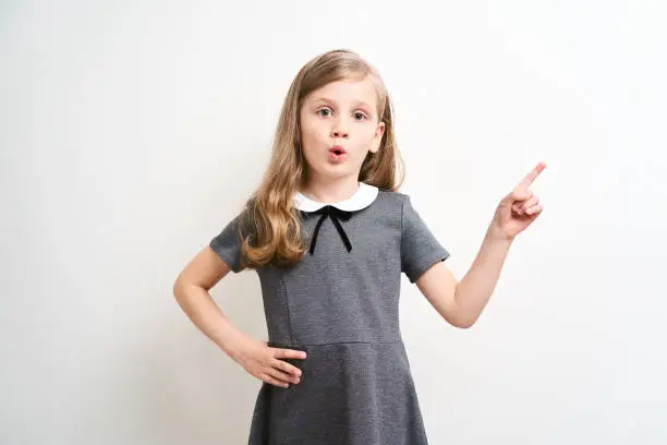 Little girl photographed against white background wearing school uniform dress isolated pointing with index finger