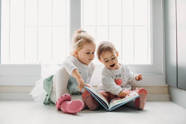 Sisters reading a book together in a window seat