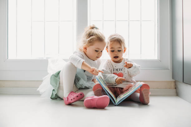 istock Sisters reading a book together in a window seat 1151486434