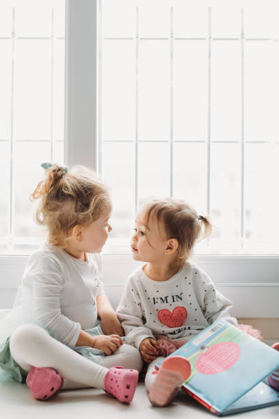 istock Sisters reading a book together in a window seat 1151486465