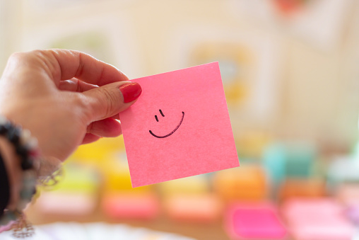 Closeup of woman's hand holding pink sticky note with smiley face