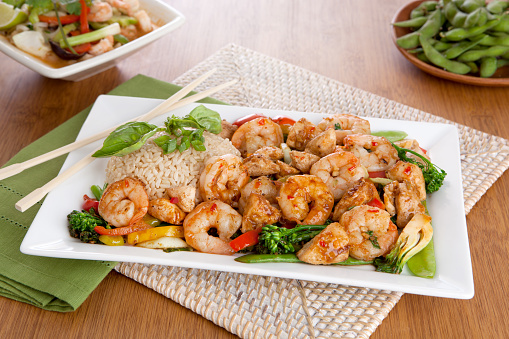 a plate of spicy Thai shrimp and chicken stir fry with rice and chopsticks