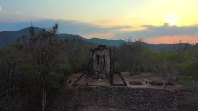 Sunset Scene of Buddha Statue on top of mountain in Sukhothai Historical Park in Sukhothai province, Thailand. Aerial view from flying drone