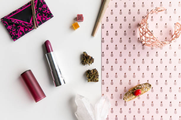 Pink Pineapples and Lipstick Woman's Accessories for Cannabis Tourism or Festival with a Joint, Nugs, and Edibles, Lipstick, Weed Pouch, Rose Gold Jewelry, in Disarray - Top Down Woman's accessories for cannabis tourism or festival with a joint, marijuana buds, and edibles with lipstick, a crystal rock, weed pouch, rose gold, on a pink pineapple background, shot top down. bud candy stock pictures, royalty-free photos & images
