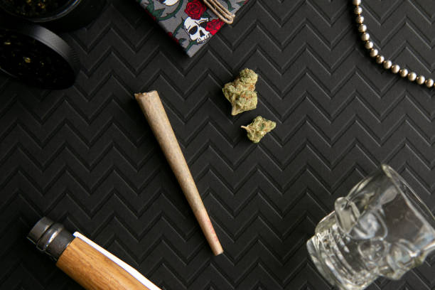 Skulls and Roses Red and Black Cannabis Scene with Marijuana, Pre-roll, Weed Grinder and Pouch, on Chevron Black Background - Top Down stock photo