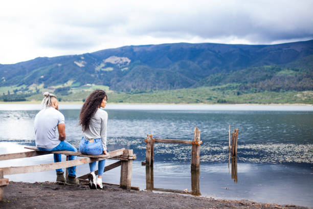 Couple of Latin race, young people, sitting by a lake, with the expression a little worried, something sad, reflecting on some topic, next to a beautiful lake, on a gray afternoon