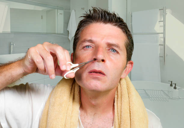 lifestyle natural portrait of young attractive and concentrated man cutting carefully hairs in his nose with small scissors at home bathroom in male beauty and domestic hygiene concept stock photo