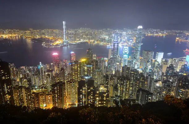 Urban sprawl and glowing skyscrapers along Victoria Harbour in Hong Kong at night.