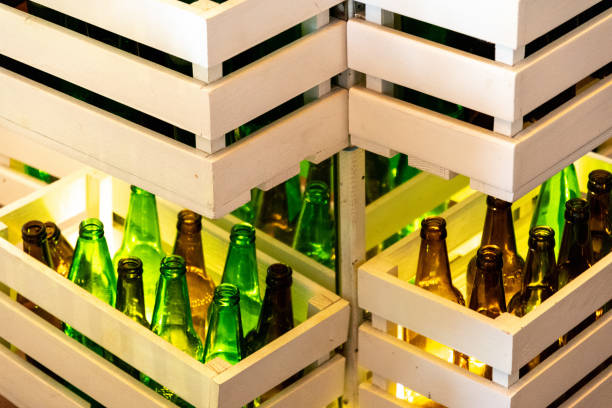 Zigzag shaped shelves made from white painted wood crates with green and brown glass bottles inside. Retro style beer bottle rows. Empty glass bottles shined by lighting. stock photo