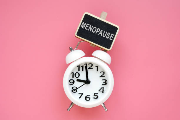 reloj despertador y menopausia de palabra sobre un fondo rosado. - menopausia fotos fotografías e imágenes de stock