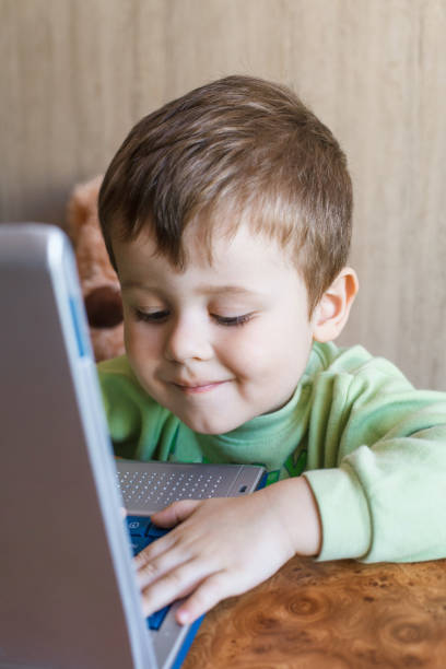istock Cute boy is pushing laptops keyboard and he is looking at the screen. 1151540419