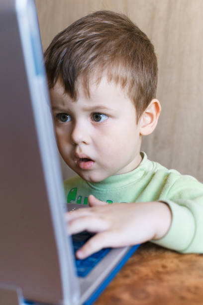 istock Cute boy is pushing laptops keyboard and he is looking at the screen. 1151540420