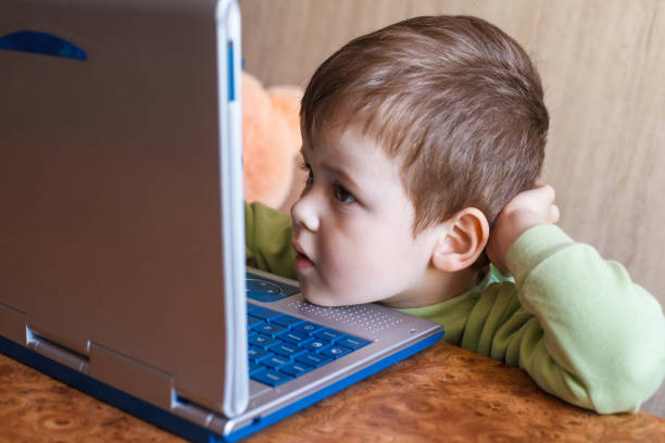 istock Cute boy is pushing laptops keyboard and he is looking at the screen. 1151540421