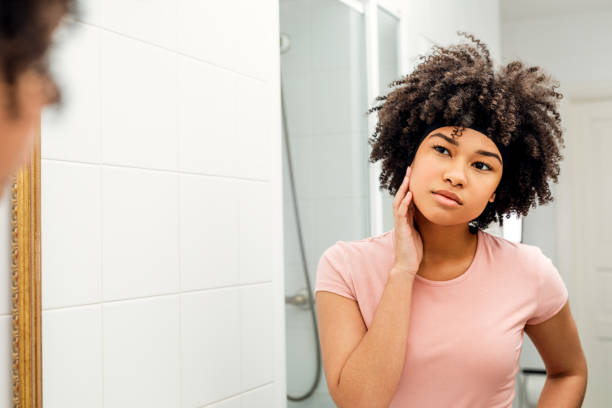 istock Young woman examining her face in bathroom mirror 1151546638