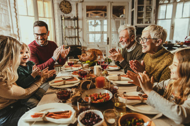 felice famiglia allargata che applaude durante il pasto del ringraziamento al tavolo da pranzo. - family american culture mother child foto e immagini stock