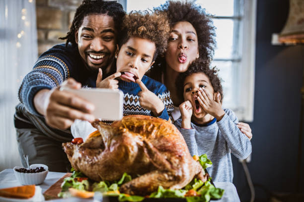 istock Happy black family making faces while taking a selfie on Thanksgiving lunch at dining table. 1151547178