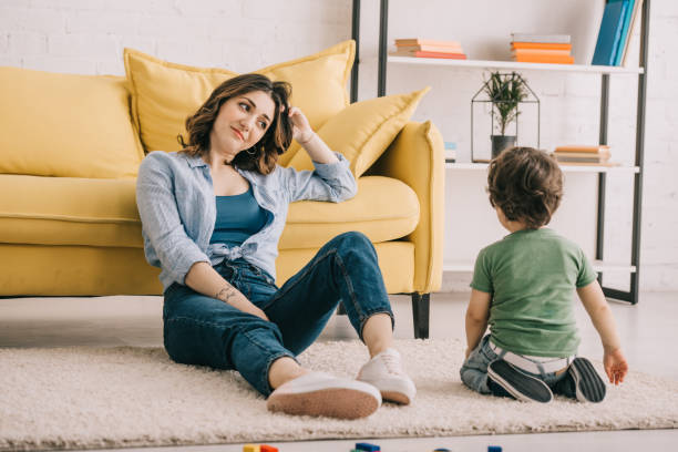 istock Tired mother sitting on carpet and looking at son 1151549644