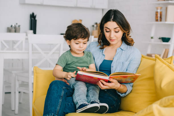 istock Mom and son sitting on yellow sofa and reading book 1151549711
