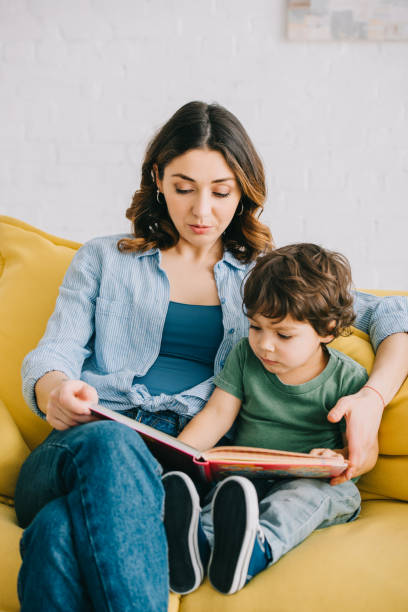istock Mom and son sitting on yellow sofa and reading book 1151549724