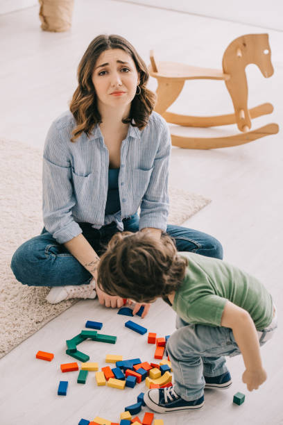 istock sad tired mother sitting on floor while son playing with toy blocks 1151549900