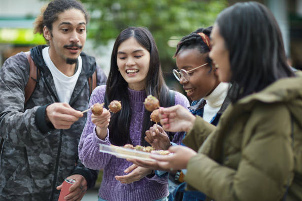 Happy friends eating parcel takoyaki in city Happy friends eating parcel takoyaki in city. Young tourists are enjoying vacation together in Tokyo. They are in casuals. takoyaki stock pictures, royalty-free photos & images