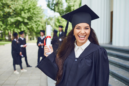 Graduate girl with a scroll in her hands smiling against the background of a group of graduates.